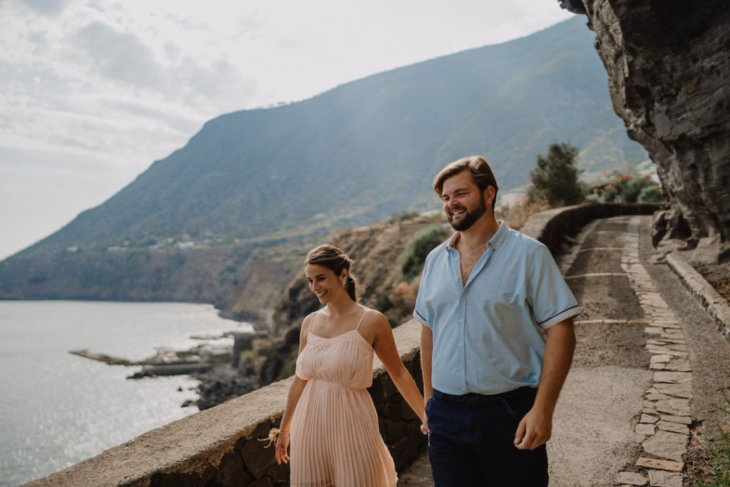 Happy couple walks on cliff path with gorgeous sea views on the island of Salina, Sicily.